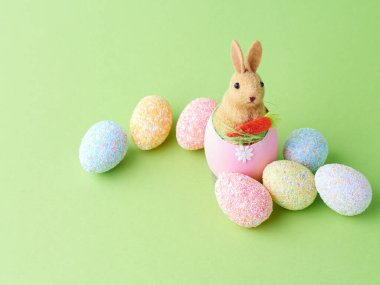 Mutlu Paskalyalar. Yeşil arka planda, kabuklu yumurtanın üzerindeki yapay sevimli tavşan. Boşluğu kopyala.