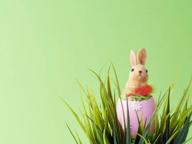 Mutlu Paskalyalar. Yeşil çimen ve yeşil arkaplan arasındaki yumurta kabuklarındaki yapay sevimli tavşan.. 