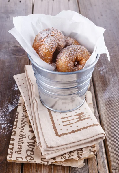 Sugar powdered cinnamon doughnuts in a metal bucket on rustic wooden background close up — Stock Photo, Image