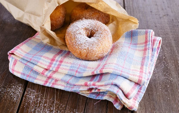 Sugar powdered cinnamon doughnuts in paper bag on rustic wooden background — Stock Photo, Image