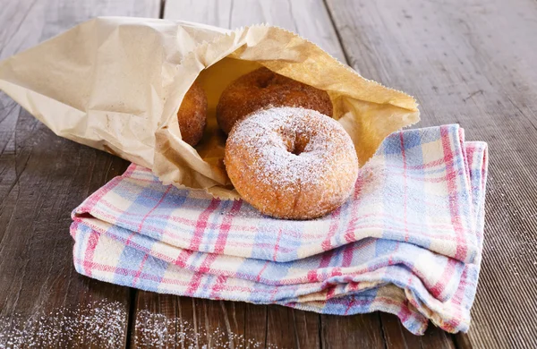 Donuts de canela en polvo de azúcar en bolsa de papel sobre fondo rústico de madera —  Fotos de Stock