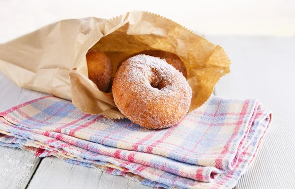 Sugar powdered cinnamon doughnuts in paper bag on white wooden background — Stock Photo, Image