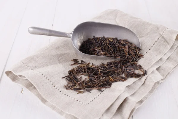 Black wild rice in a metal scoop on a white wooden background — Stock Photo, Image