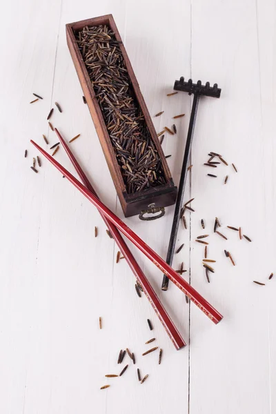 Black wild rice in a wooden box with chopsticks on a white wooden background — Stock Photo, Image