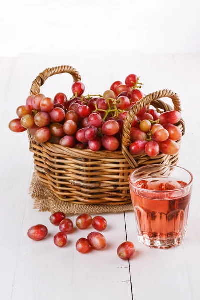 Красный виноград в тканой корзине со стаканом сока — стоковое фото