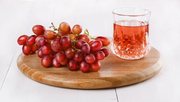 Uvas vermelhas em tábua de cortar com copo de bebida spritzy — Fotografia de Stock