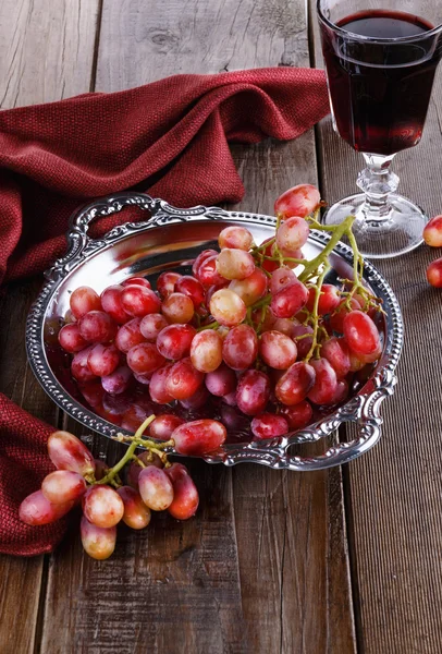 Uvas vermelhas em uma bandeja vintage com copo de vinho — Fotografia de Stock