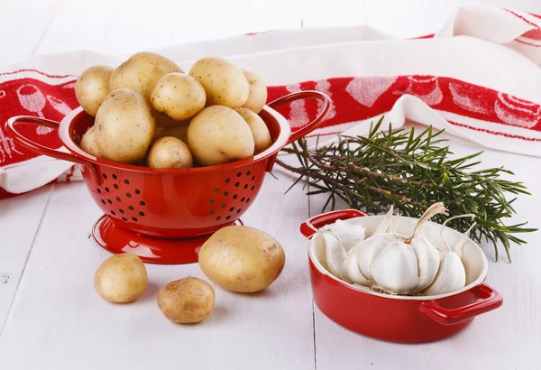 Batatas orgânicas frescas, alecrim e alho sobre ba de madeira branca — Fotografia de Stock