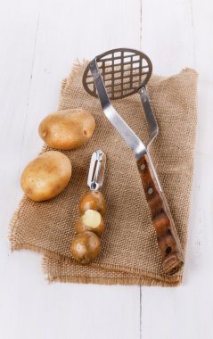Potato utensils and potato on white wooden background clipart