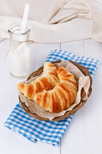 Fresh baked croissants on woven plate over white wooden backgrou — Stock Photo, Image