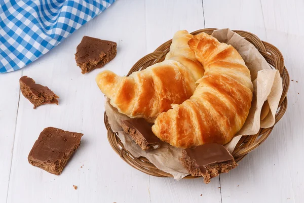 Croissants recién horneados en placa tejida sobre fondo de madera blanca —  Fotos de Stock