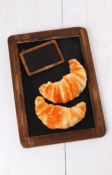 Two croissants on a black board over white wooden background — Stock Photo, Image