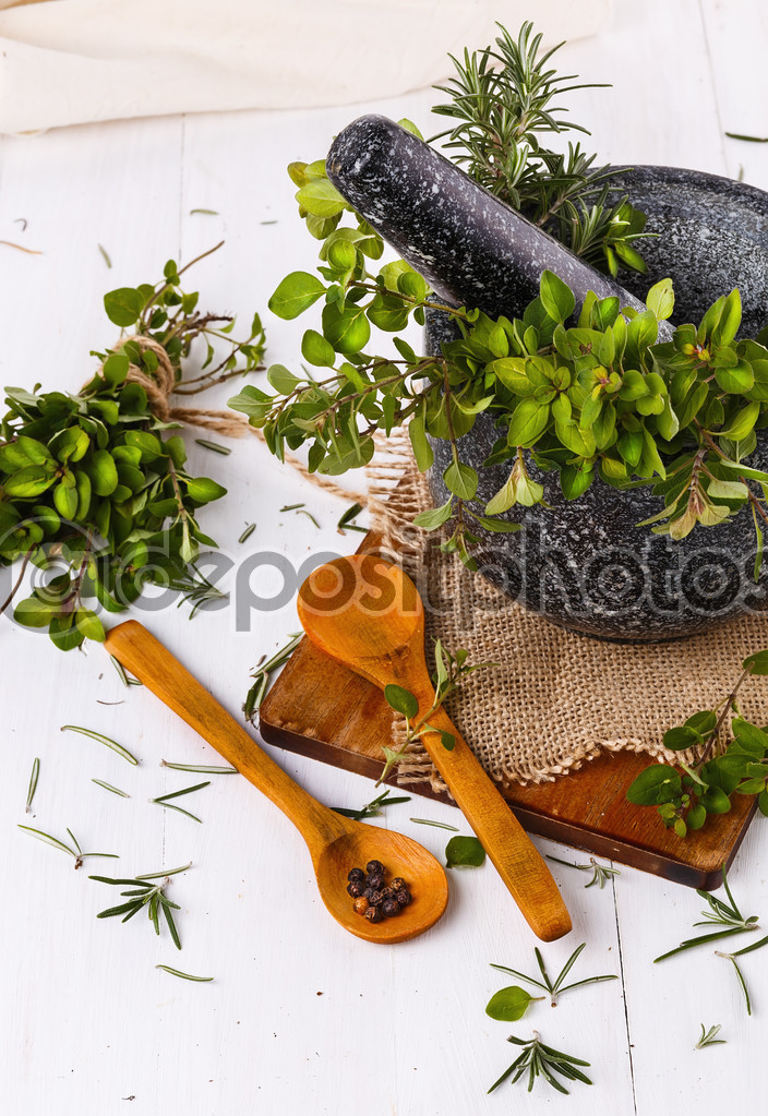 Fresh thyme and rosemary in mortar over white wooden background