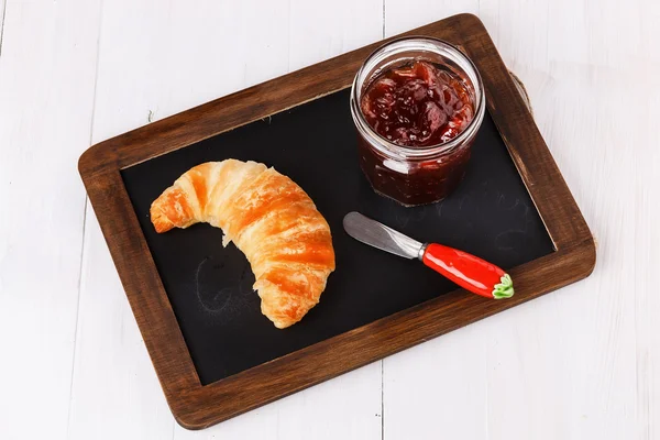 Croissant and jam on black board over white wooden background — Stock Photo, Image