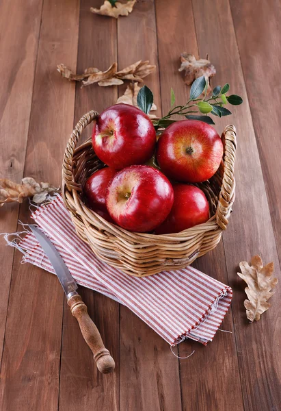 Красные яблоки в плетеной корзине на деревянном фоне — стоковое фото