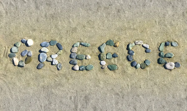 Photo of a single word Greece arranged with various small pebbles on a beach sand