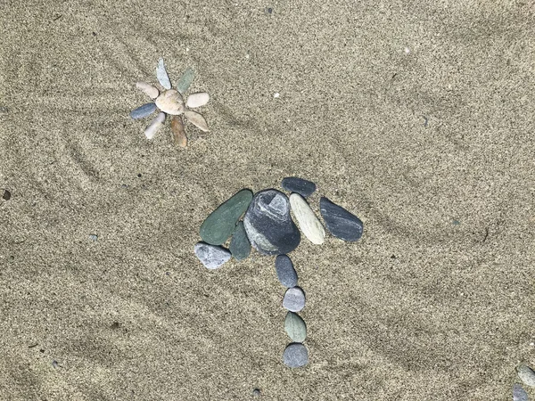 A composite image of small multicolor pebbles arranged on a sand beach show sun and parasol