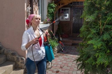 Sarışın, orta yaşlı kadın bahçesinde meyve suyu püskürtücüsü kullanıyor..