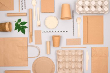 Gri arka planda farklı çevre dostu sofra takımı ve Kraft kağıt gıda ambalajları. Sokak yiyecekleri ambalajı, fincanlar, tabaklar, pipetler, kaplar ve kese kağıtları. Model, düz yat.