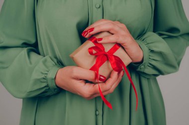 Elinde kırmızı kurdeleyle süslenmiş Noel hediyesi kutusu tutan genç bir kadın. Noel tatili, yeni yıl kutlaması konsepti. Noel için aile hediyeleri hazırlıyorum.