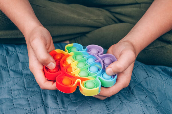 Front view on boys hands playing with rainbow pop it fidget toy. Push bubble fidget sensory toy - washable and reusable silicone stress relief toy. Antistress toy for child with special needs