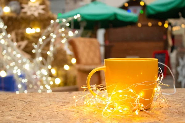 Tazza gialla con luci di illuminazione intorno. Mercatino di Natale con sfondo illuminante, spazio copia — Foto Stock