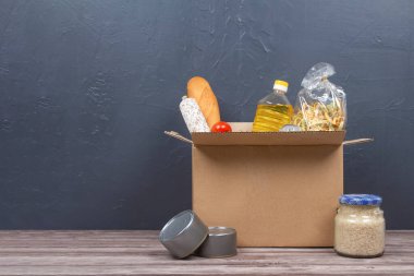 Yemek bankası, yemek teslimatı konsepti. Bağış kutusunda farklı gıda bağışları var. Arka planda da farklı şeyler var. Makarna, taze sebzeler, konserve yiyecekler, baget ekmeği, pişirme yağı. Model