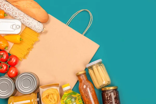 Food bank, food delivery concept. Food donations and paper bag on green background with copy space - pasta, fresh vegatables, canned food, baguette and other groceries. Mockup