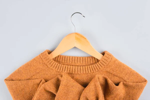 Wooden hangers with orange sweater on gray background with copy space. Clothing donations, conscious and environmentally friendly consupmtion - new trends in shopping. Slow fashion concept