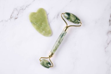 Yeşim yüz silindiri ve beyaz mermer masa arka planında gua sha aracı. Doğal taşlardan yapılan masaj terapisi için yüz masajı kiti, yaşlanma önleyici aletler..