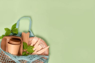 Düz bir zemin üzerinde Kraft kağıt yemek fincanları, tabaklar ve ahşap çatal bıçaklı kaplar vardı. Mavi pamuk çantanın içinde açık yeşil arka planda fotokopi alanı vardı. Sokak yiyecekleri ambalaj konsepti. Çevre dostu sofra takımı