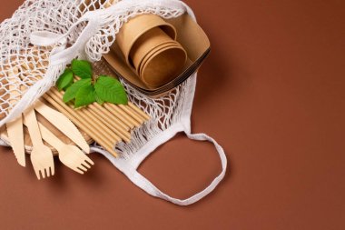 Kraft kağıt yemek fincanları ve üzerinde tahta çatal bıçak seti olan kahverengi arka planda beyaz pamuklu çanta ve fotokopi alanı - çevre dostu sofra takımı. Sokak yemekleri kağıt ambalajlarını kaldırır.