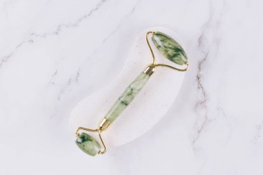 Yeşim yüz silindiri ve beyaz mermer masa arka planında gua sha aracı. Doğal taşlardan yapılan masaj terapisi için yüz masajı kiti, yaşlanma önleyici aletler..