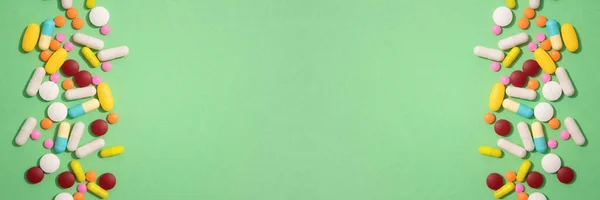 Banner with assorted multicolored medicine pills, capsules and tablets on light green background with copy space. Variety of immune system vitamins. Dietary bio supplements. Selective focus