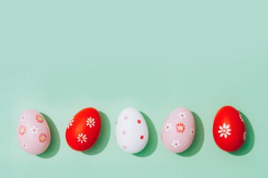 Easter greeting card - bright red and pink Easter eggs on pastel mint background with copy space for your text. Flat lay. Selective focus