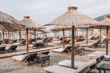 Budva 'da güneşli deniz yatakları ve plaj şemsiyeleri, Adriyatik kıyılarının manzarası, yaz turizm sezonu, turistlerin olmadığı boş deniz plajı.