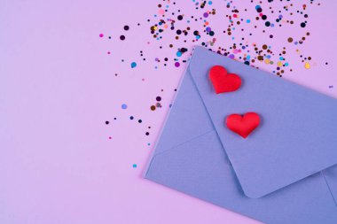 Sevgililer Günü arkaplanı. Üzerinde kırmızı kalpler ve pembe arka planda fotokopi alanı olan konfeti olan mor bir zarf. Düz yerde, üst tarafta. Tebrik kartı, davet