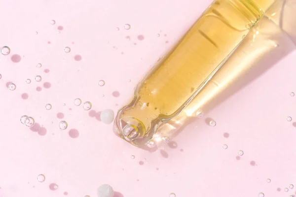 Pipetta con siero o gel giallo liquido su fondo in vetro rosa chiaro. Il concetto cosmetico di bellezza. Vista dall'alto — Foto Stock