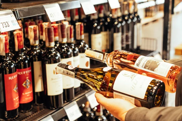 Lviv,ウクライナ- 2022年2月20日:不良少年店,顧客読書ワインラベルとアルコール店で完璧な白または赤ワインのボトルを選択します。 — ストック写真