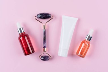Yüz masajı seti. Güzellik yüz serumlu ametist gua sha roller. Kozmetik yağ ve pembe arka planda yüz nemlendirici kremi. Yüz silindiri, doğal taşlardan yapılmış masaj aleti. Seçici odak
