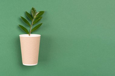 Yeşil yapraklı Kraft kağıt kahve fincanı. Sıcak içecekler için ayrıştırılabilir, gübrelenebilir kağıt kap. Yeşil arka planda fotokopi alanı olan kağıt bardak. Çevre koruma kavramı. Seçici odak