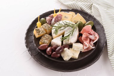 Peynir, salam ve jambonlu Charcuterie tahtası. Beyaz masa arkasında siyah tabakta servis edilen zeytinlerle birlikte. İtalyan geleneksel pastası.