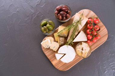 Peynir dilimli şarküteri tahtası. Brie, mavi peynir, gorgonzola, farklı antipastalarla peynirli camembert zeytin, vişneli domates, yağlı enginar. Boşluğu gri taş arkaplanda kopyala, düz yatay