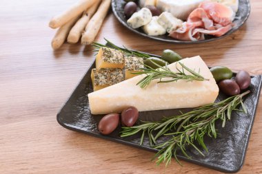 İtalyan antipasti, peynirli pano peyniri ve jambonlu şarküteri tahtası yanında zeytin ve siyah tabakta Grissini servis ediliyor.