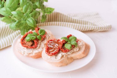 Geleneksel İtalyan aperatifi - bruschetta veya ricotta peynirli tost ve beyaz masa arkasında fesleğenle kaplanmış güneşte kurutulmuş domates. Lezzetli İtalyan aperatifi