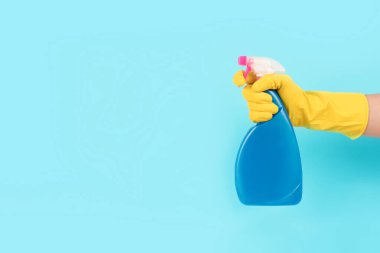 Sarı koruyucu lastik eldiven, elinde deterjan şişesiyle mavi arka planda fotokopi alanı olan bir eldiven. Farklı mutfak ve banyo yüzeyleri için temizlik malzemesi. Temizlik hizmeti konsepti. Model