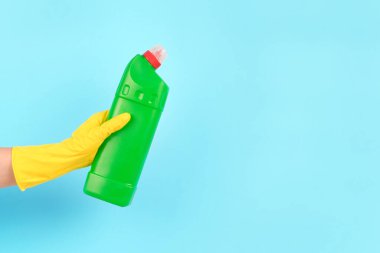 Sarı koruyucu lastik eldiven, elinde yeşil sprey şişesiyle mavi arka planda fotokopi alanı olan deterjan. Farklı banyo yüzeyleri için temizlik malzemesi, tuvalet dezenfektanı. Temizlik hizmeti konsepti. Model