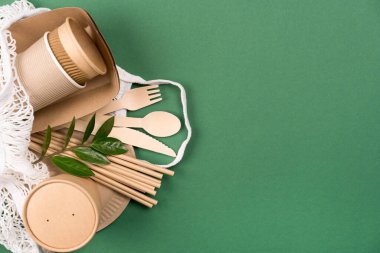 Kraft kağıt yemek fincanları, tabaklar ve kaplar beyaz pamuk torbalarda yeşil arka planda fotokopi alanı ile. Sokak yemekleri kağıt çatal bıçakları götürür. Bardaklar, tabaklar, pipetler, ahşap çatal bıçaklar.
