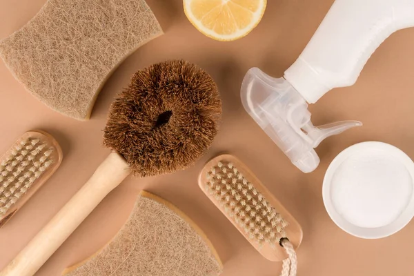 Green cleaning concept. Flat lay composition with natural household cleaners kit with bamboo brushes, organic dishcloth, lemon, baking soda, spray bottle with cleaning liquid or organic citrus air freshener on beige background. Mockup