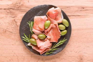 Tahta masada zeytinli proscuitto ile servis edilen şarküteri tahtası. Geleneksel İtalyan antipastası ile siyah tabak. Seçici odak